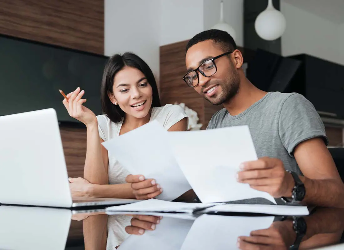 Annuities-Cheerful-Young-Couple-Using-a-Laptop-Together-at-the-Kitchen-Table-While-Analyzing-Financial-Documents