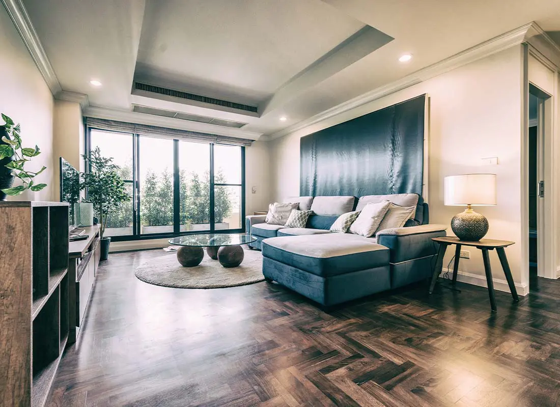 Condo-Insurance-Modern-View-of-a-Living-Room-In-an-Upscale-Condo-With-Large-Windows-Leading-to-a-Balcony-With-Foliage-at-Dusk