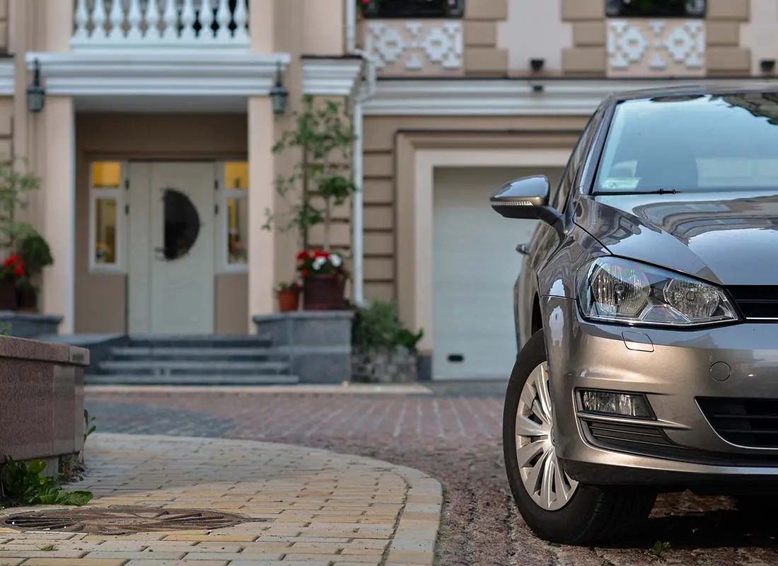 Home-and-Auto-Insurance-Bundled-Close-up-View-of-a-Luxury-Car-Parked-in-Front-of-a-Large-Modern-Home-Blurred-in-the-Distance