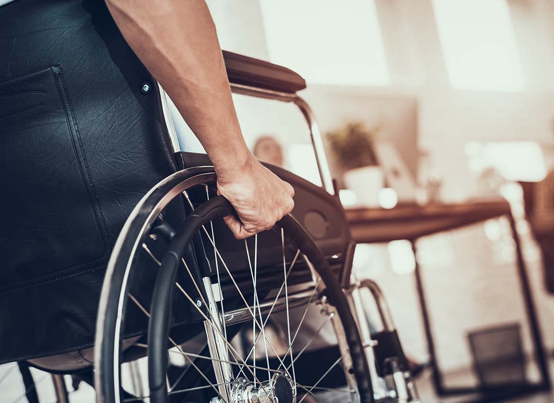 Long-Term-Disability-Insurance-Close-up-of-a-Man-Using-a-Wheelchair-in-the-Doctors-Office-with-the-Reception-Desk-Area-in-the-Distance
