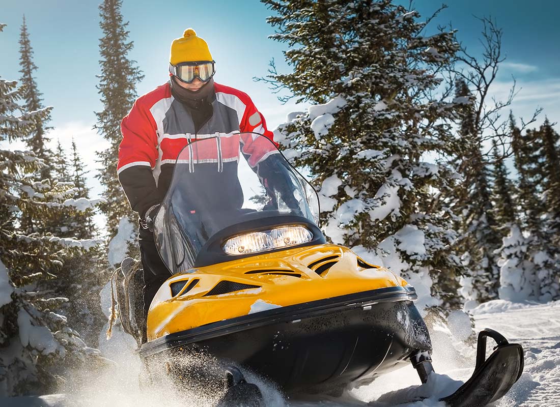 Snowmobile-Insurance-Close-up-of-a-Man-in-Winter-Attire-and-Goggles-Riding-a-Snowmobile-Through-Snow-and-Trees-on-a-Winter-Day